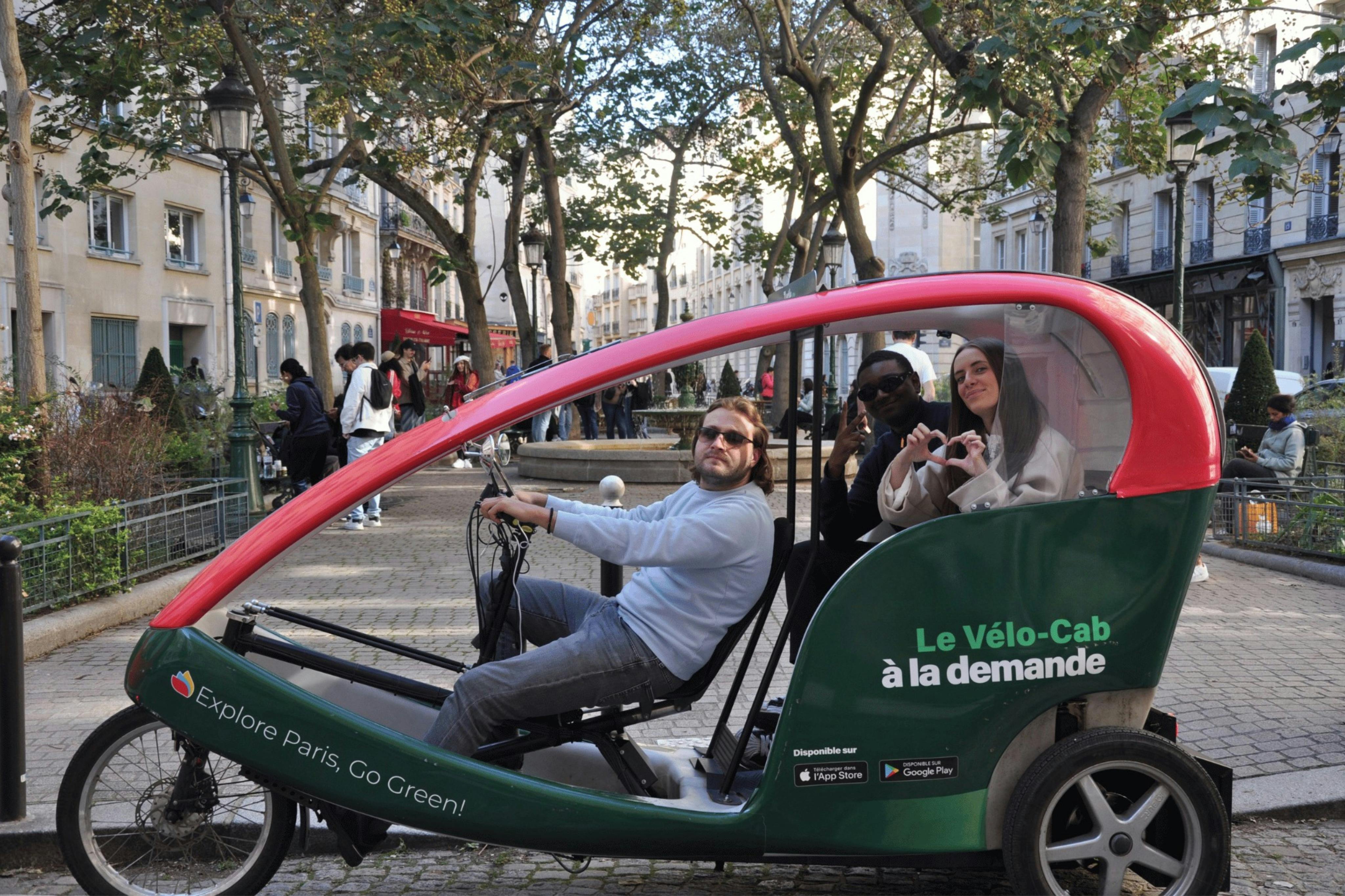 Three people sit in a green and red pedicab labeled "Le Vélo-Cab à la demande," parked on a tree-lined street with buildings.