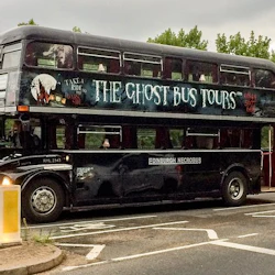 En svart dubbeldäckare märkt "The Ghost Bus Tours" och "Edinburgh Necrobus" parkerade på en gata med träd i bakgrunden.