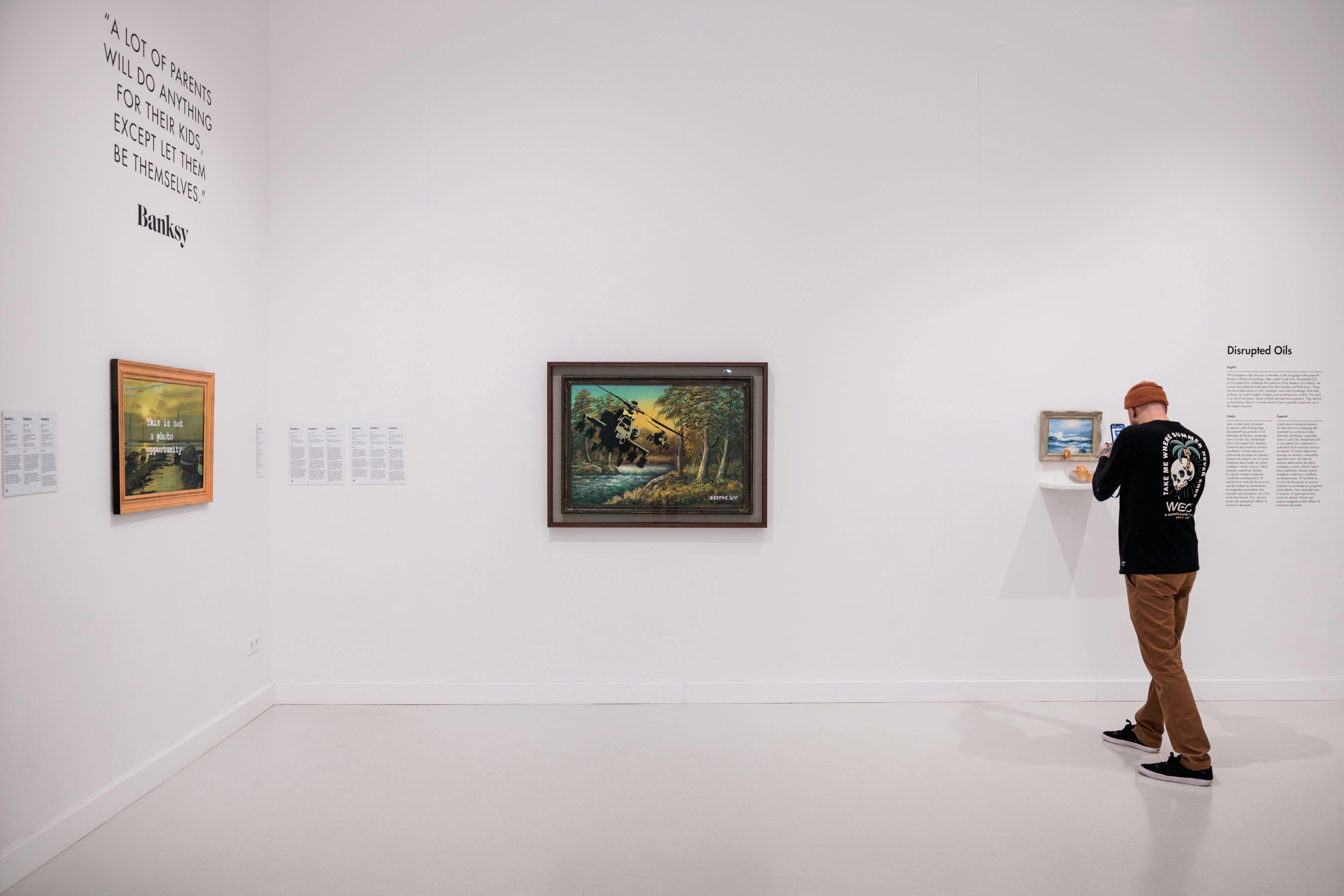 Ein minimalistischer Galerieraum mit zwei Gemälden an einer weißen Wand. Auf der rechten Seite ist eine Person teilweise sichtbar.