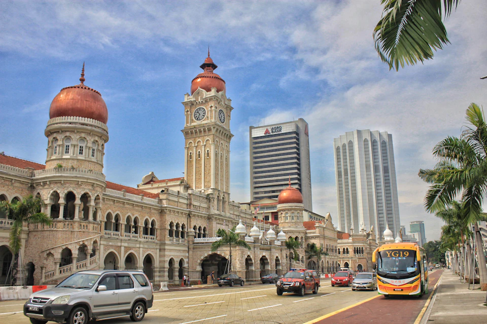 Busy city street with cars in front of a historical building with domes and a clock tower, set against modern high-rises.