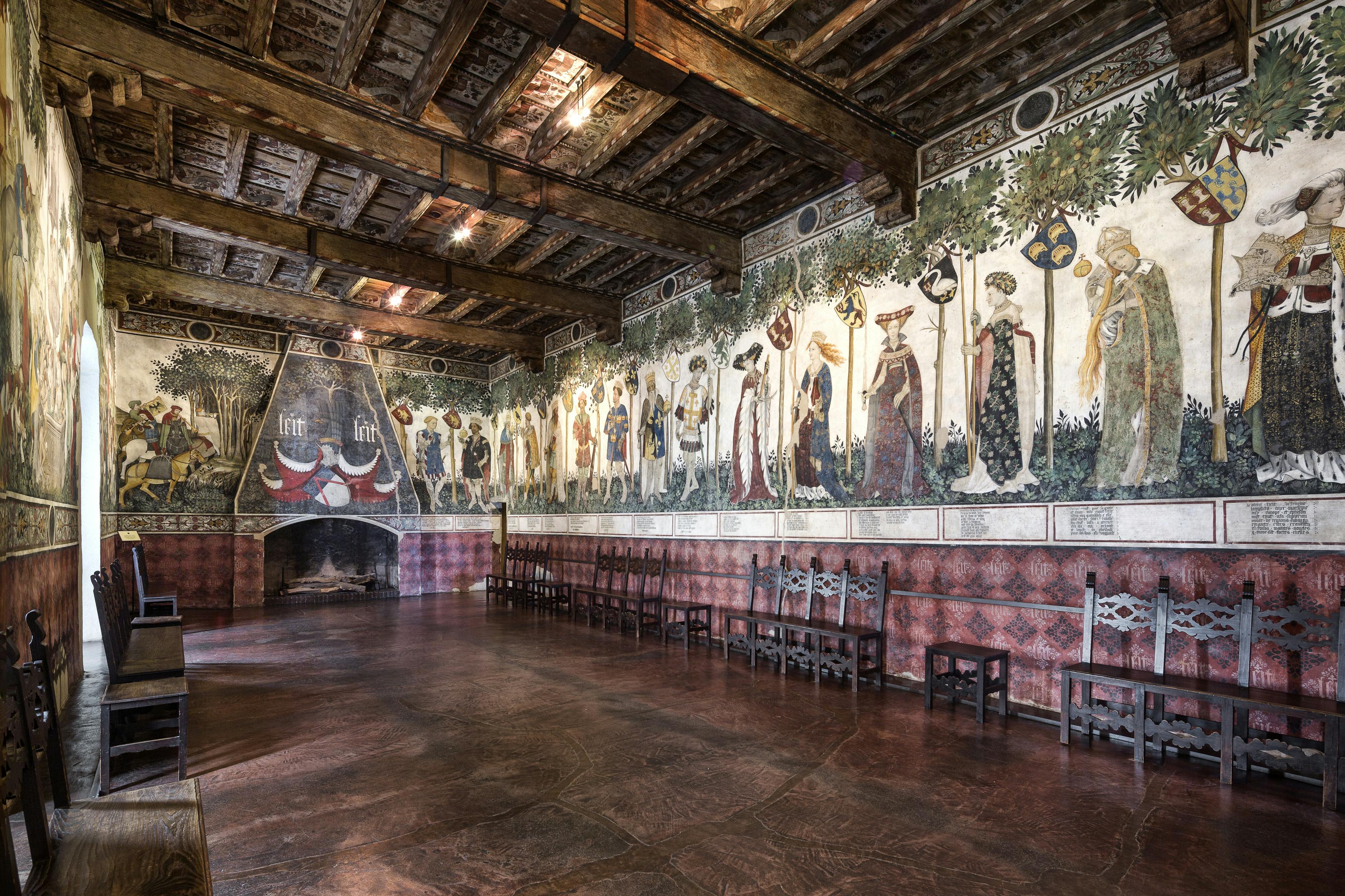 这座历史悠久的大厅设有木梁、墙壁上挂着中世纪人物壁画、大壁炉和成排的木椅。