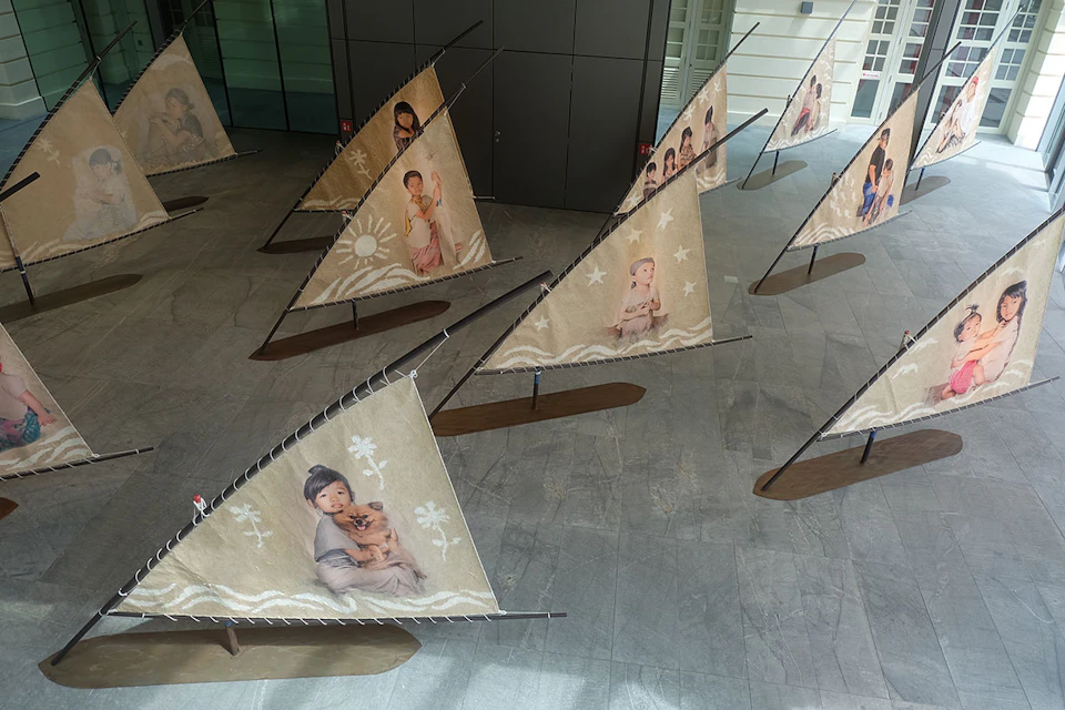 Multiple triangular sails displayed indoors feature images of children in various poses, mounted on wooden bases.