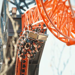 Människor kör en berg- och dalbana med ett orange spår som vänder upp och ner. Träd och blå himmel syns i bakgrunden.