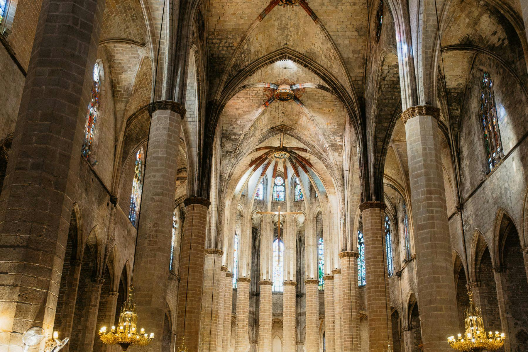 Interior de uma catedral gótica com tectos altos abobadados, colunas de pedra, vitrais e candelabros.