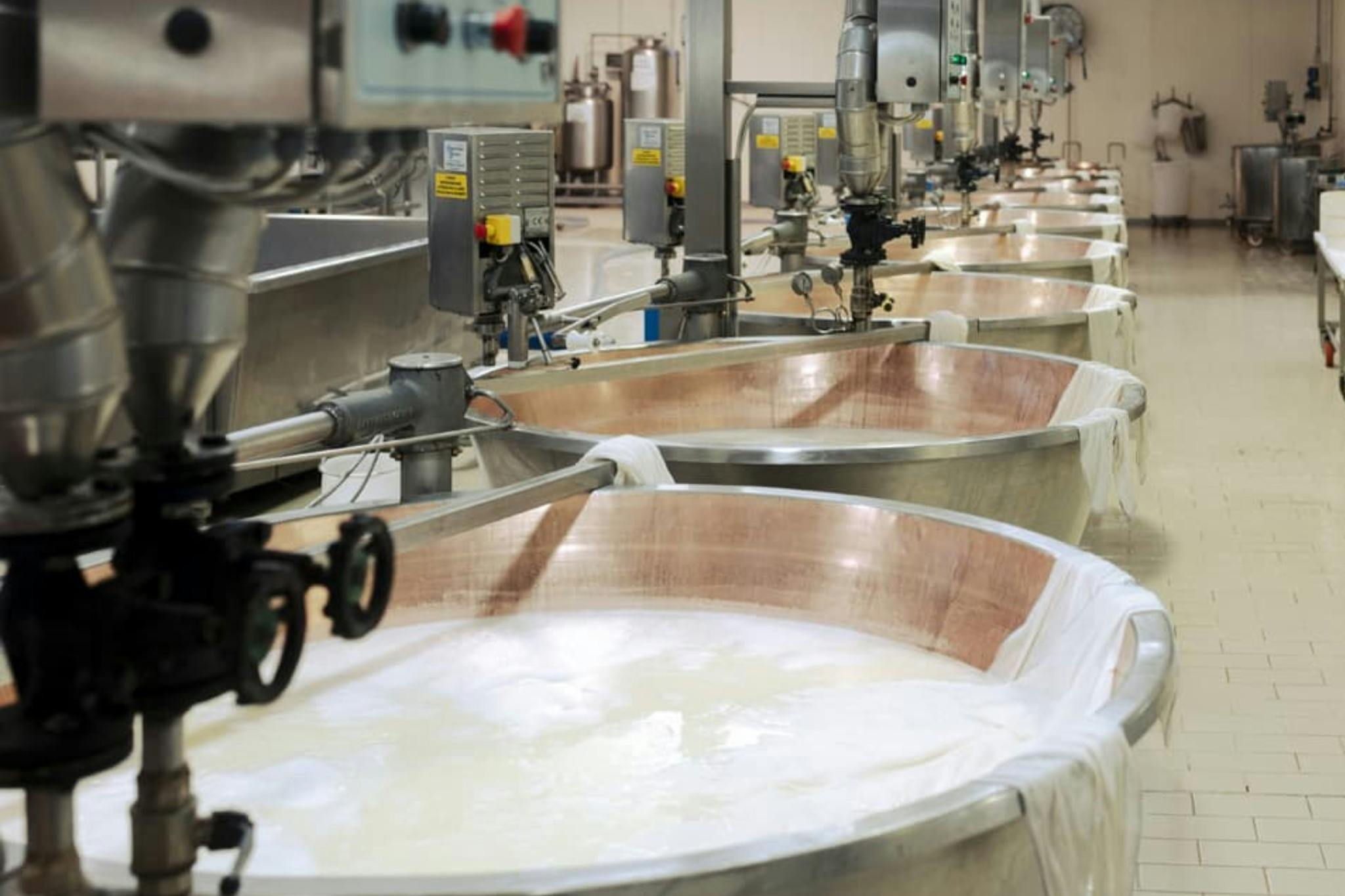 Grandi vasche di metallo piene di liquido in un ambiente industriale, con diversi macchinari e tubi sopra i contenitori.