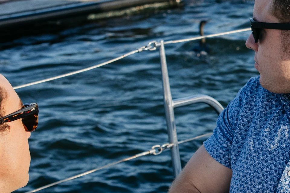 Two young males sitting on a sailboat turning to watch the sea lions lounging behind them