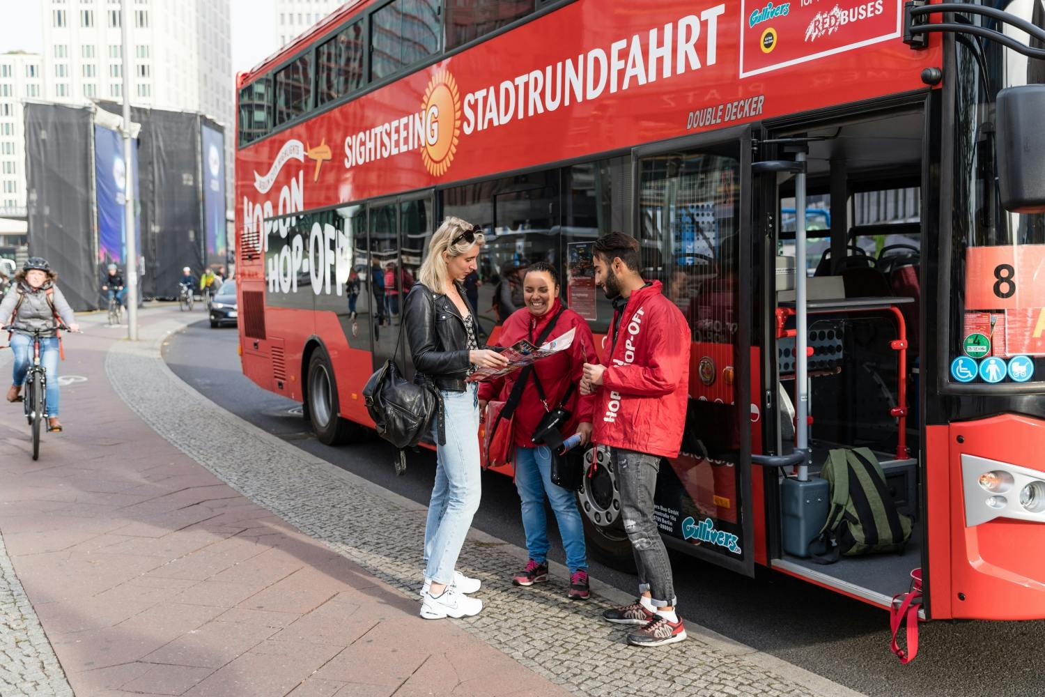 Trois personnes se tiennent à côté d'un bus touristique rouge à impériale. Une personne tient une carte et discute avec deux membres du personnel.