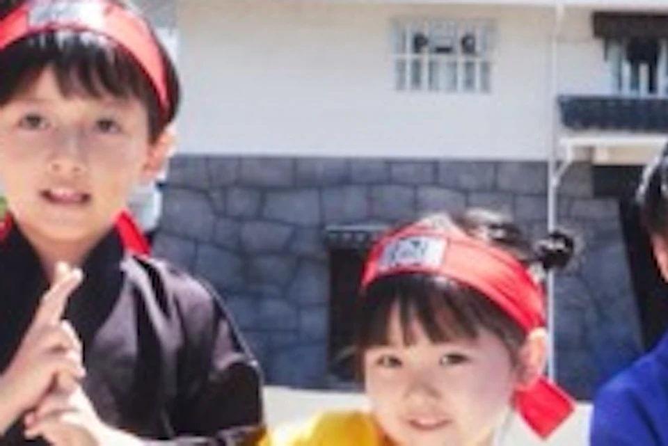 Five children in colorful traditional outfits pose playfully on a sunny street lined with traditional Japanese buildings.