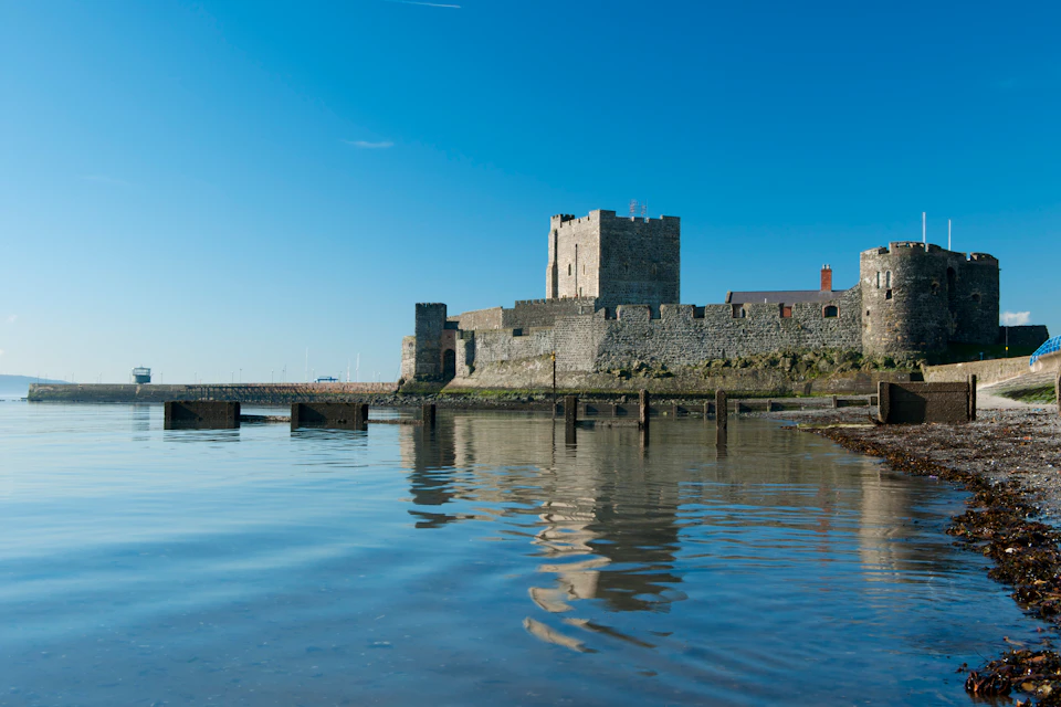 Stone fortress with towers reflecting in calm water under a clear blue sky.