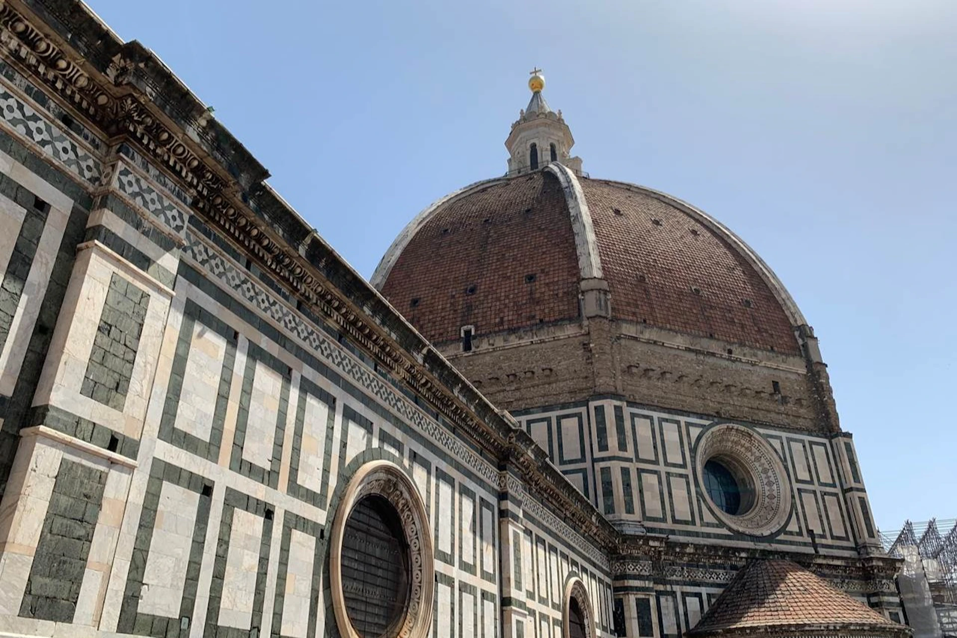 The dome of Florence's Cathedral with its marble facade and circular windows under a clear blue sky.