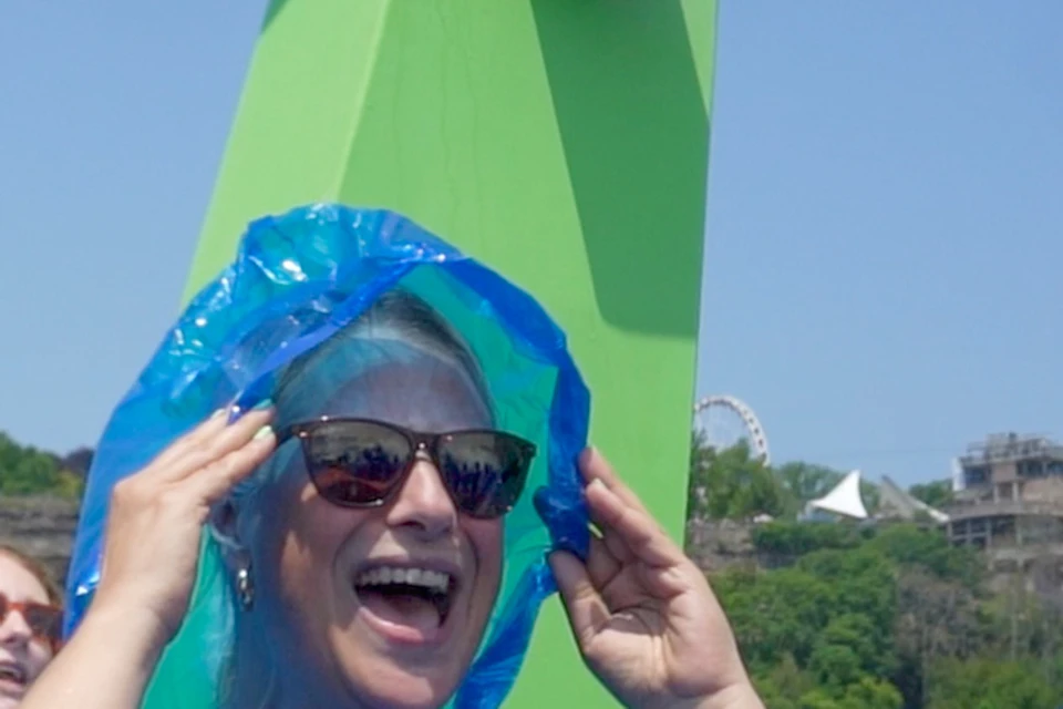 People wearing blue ponchos and sunglasses, smiling and laughing with greenery and a green structure in the background.