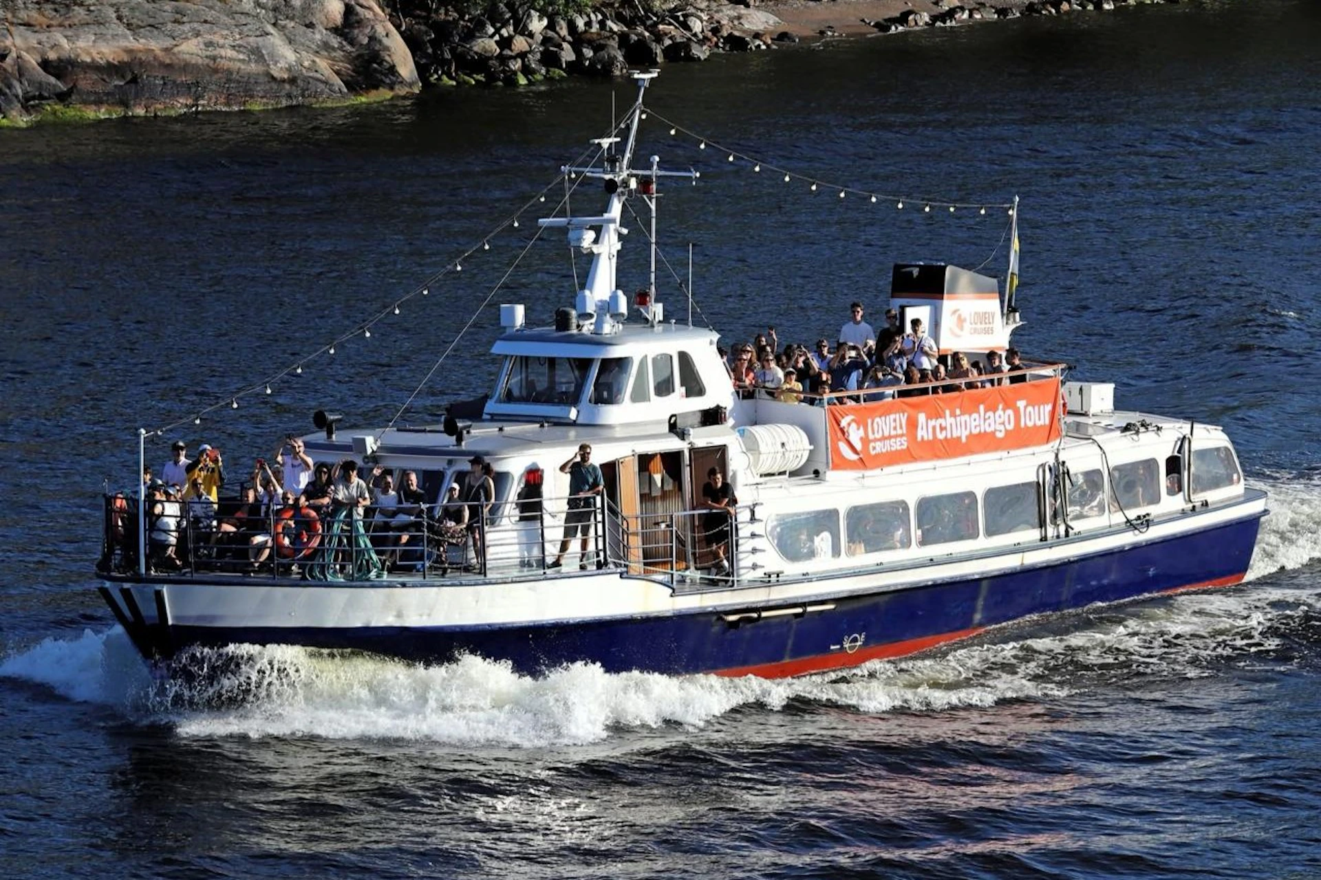 A tour boat with passengers on the deck cruises through the water, with a sign reading 'Archipelago Tour' visible.