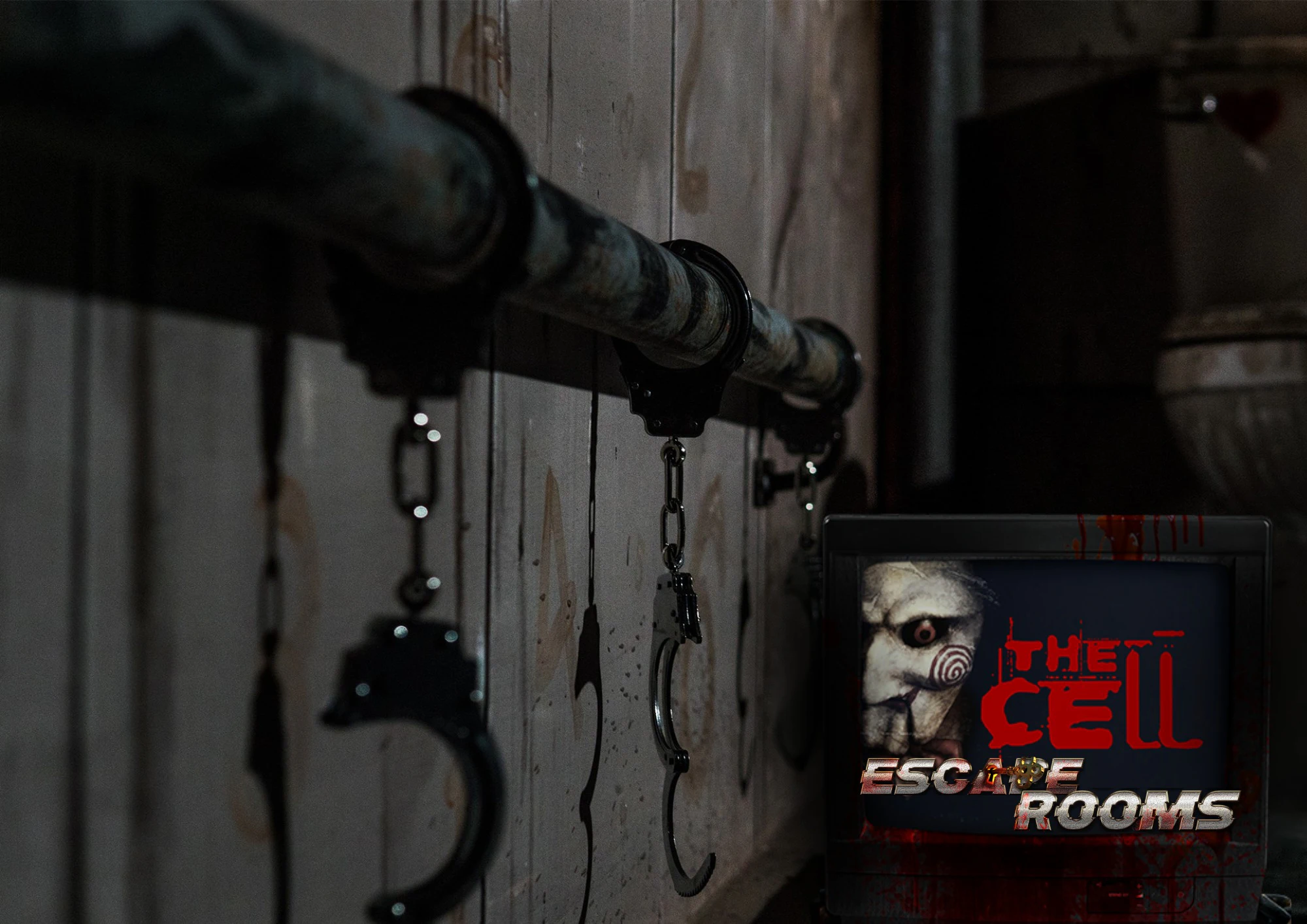 A dimly lit room with handcuffs attached to a metal pipe on the wall and a sign reading 'The Cell Escape Room.'