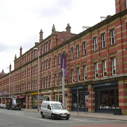 En gata kantad av röda tegelbyggnader med butiker, bilar parkerade längs sidan och en skåpbil som körde längs vägen.