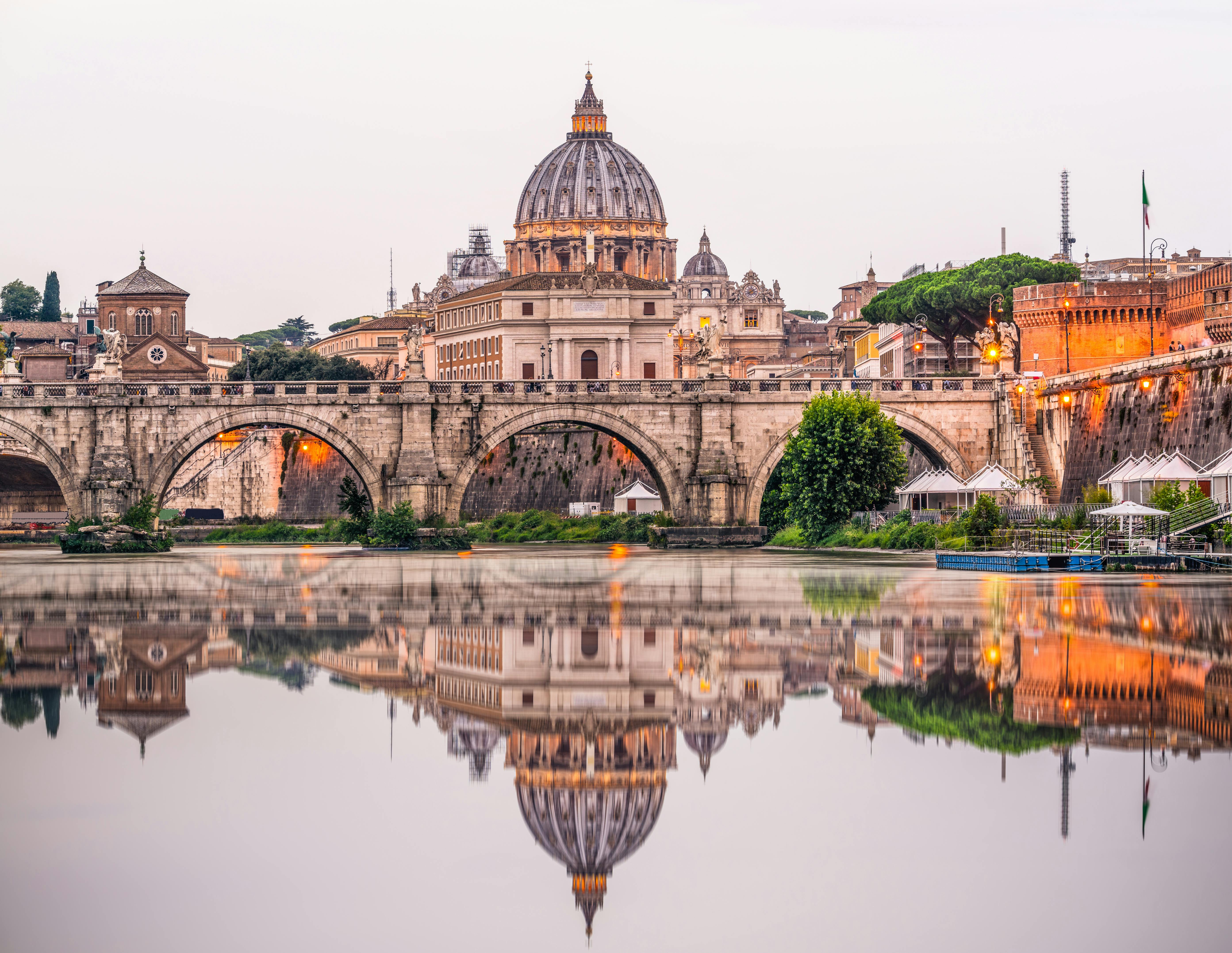 Il ponte storico e la cupola della Basilica di San Pietro si riflettono in un fiume tranquillo, illuminato dalle luci della sera.