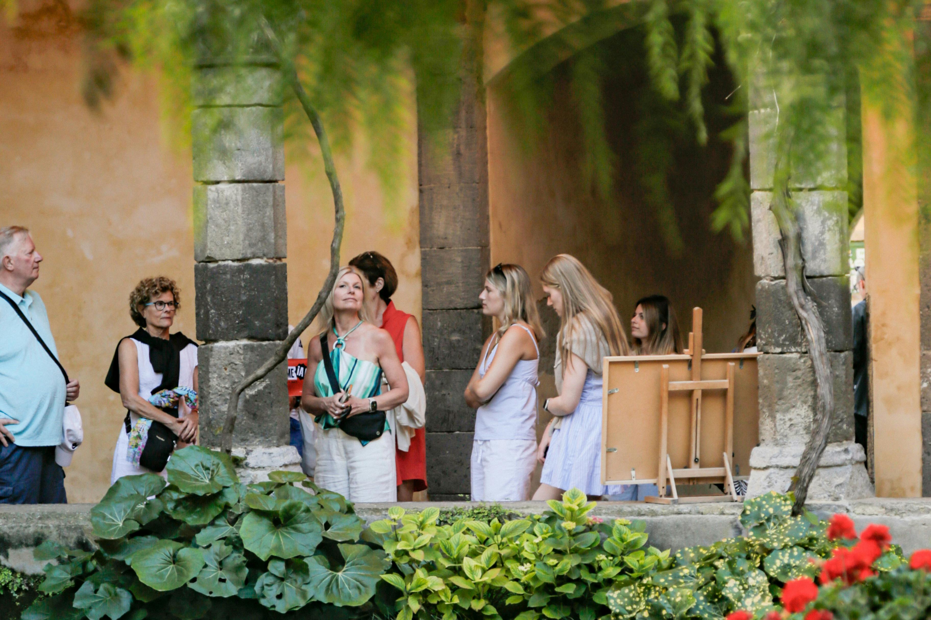 Mensen staan op een binnenplaats met weelderig groen en stenen zuilen op de achtergrond.