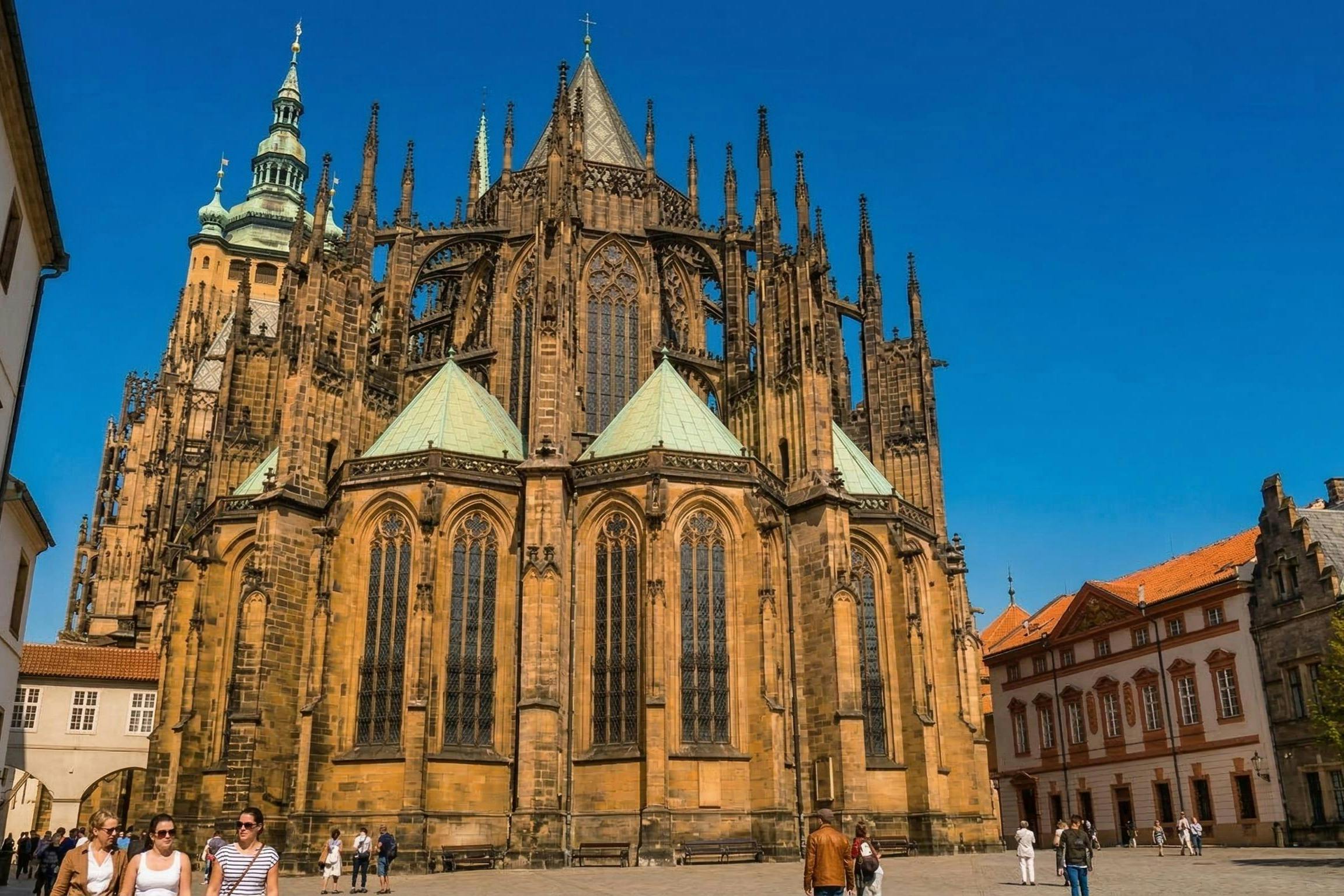 A Gothic cathedral with intricate details and pointed spires under a blue sky, with people walking in the foreground.