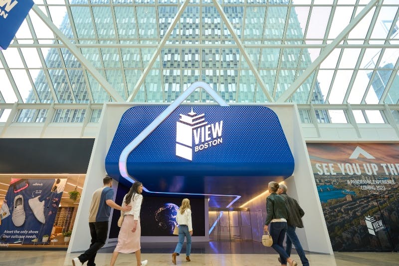People walking in a modern, glass-covered atrium with a &#34;View Boston&#34; entrance, displaying an illuminated sign.