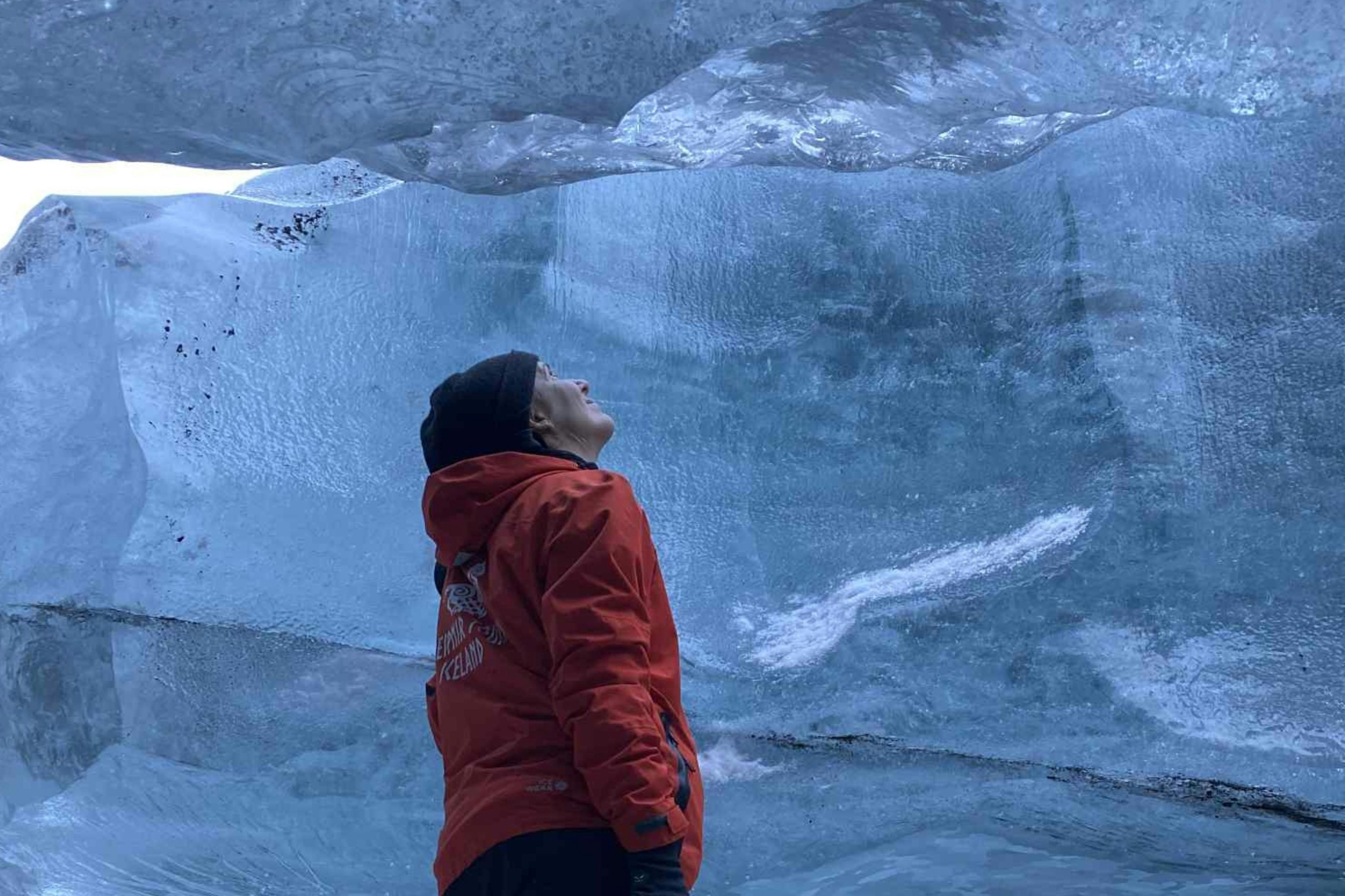 Una persona con una giacca rossa e un cappello nero guarda una grande formazione di ghiaccio sopra di loro.