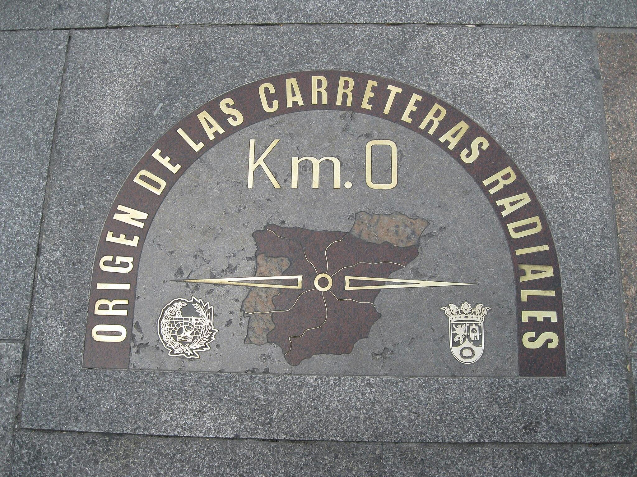 Targa semicircolare a terra che segna il "Km 0", l'origine delle autostrade radiali spagnole, con una mappa e gli emblemi ufficiali.