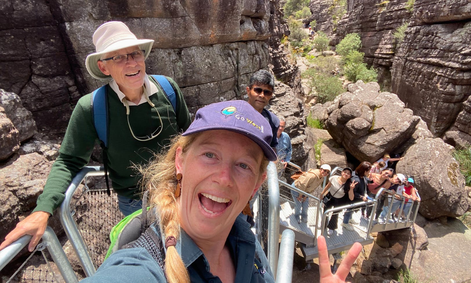 一群人在岩石徒步道上微笑。 前面的女子自拍，其他人在她身后爬楼梯。