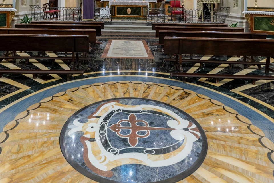 Intricate marble floor design in a church, with pews, an altar, and a decorative railing in the background.