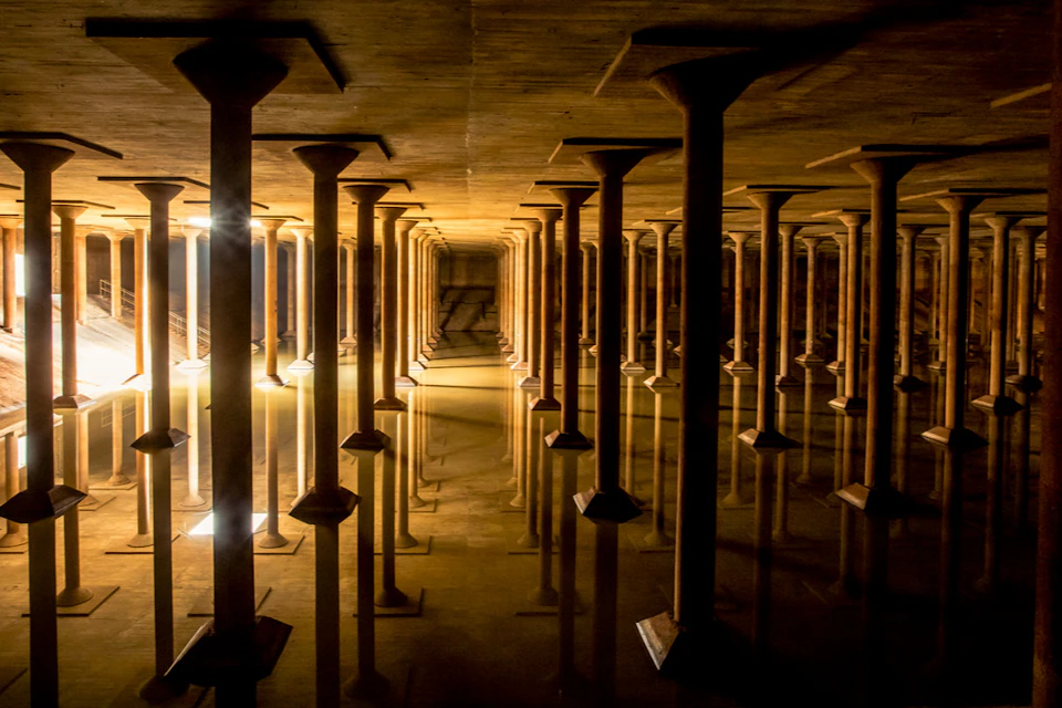 A dimly lit underground structure with rows of columns reflected in standing water on the floor.