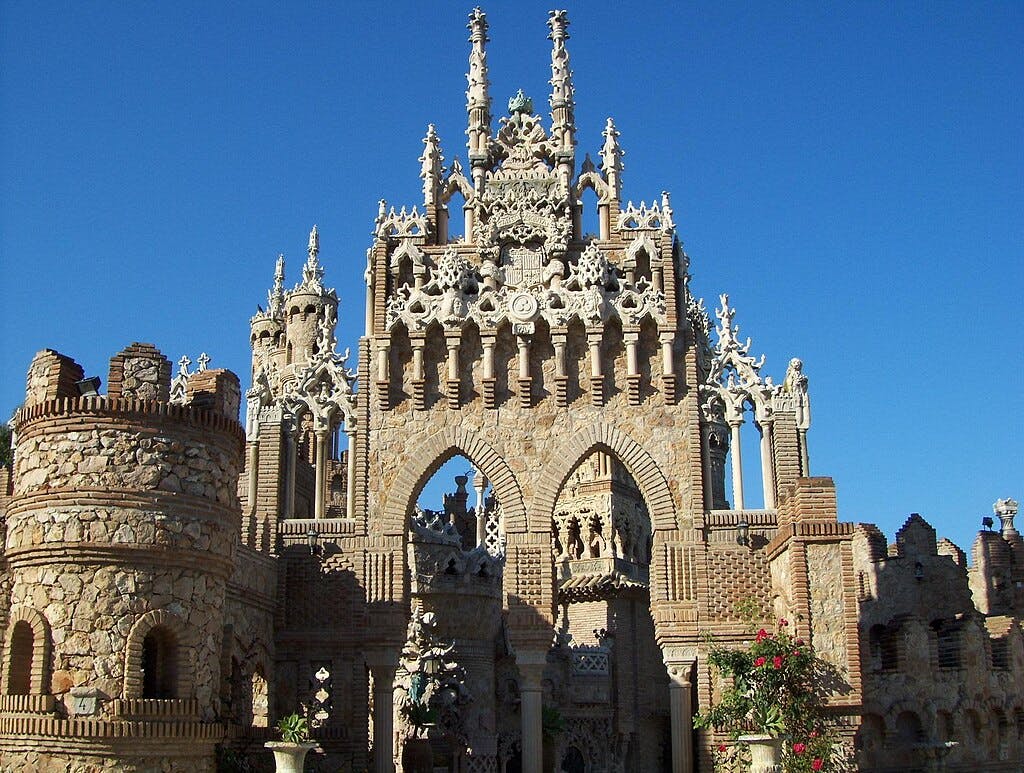 Ornate stone and brick castle with Gothic-style arches and towers under a clear blue sky.
