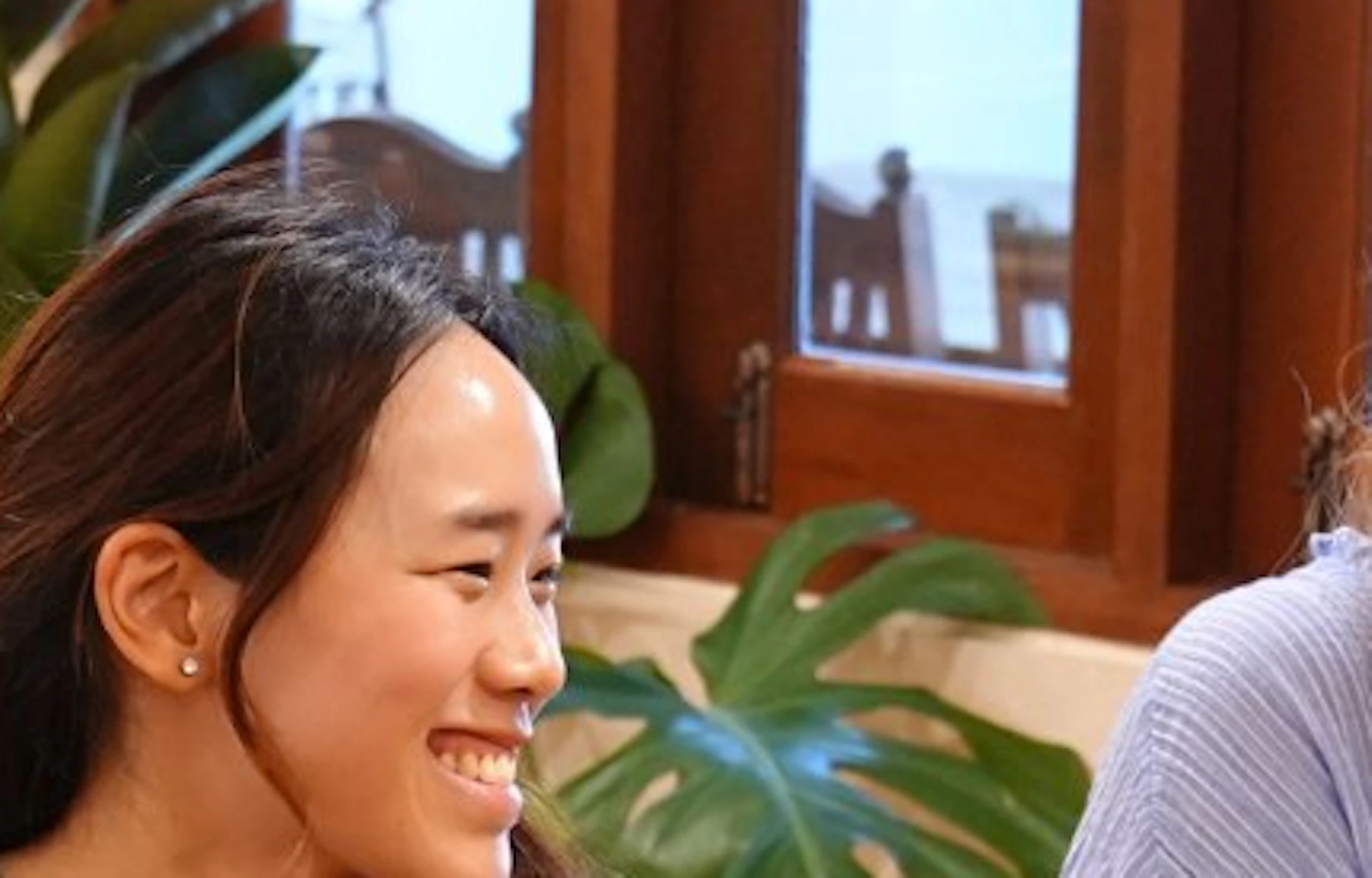 Three people sitting at a table with baskets of fresh vegetables in a kitchen setting, smiling and conversing.