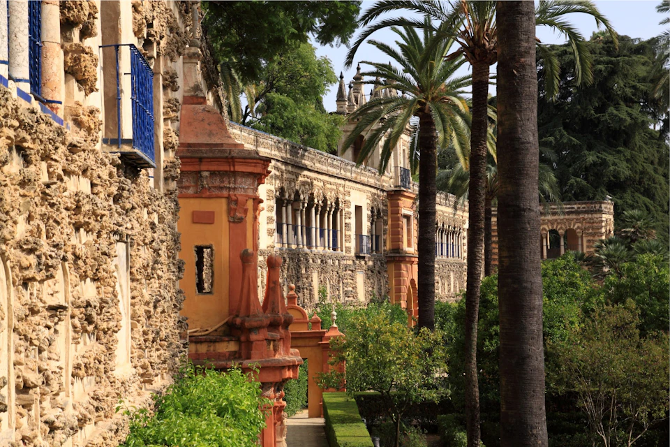 A historic building with ornate architecture surrounded by gardens and tall palm trees on a sunny day.