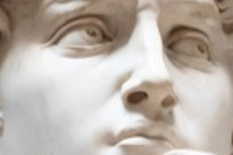 A marble statue of a nude man with detailed curly hair, positioned in an ornate room with a high, light-colored ceiling.