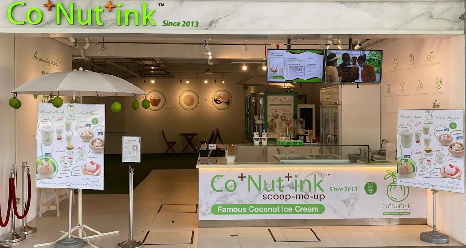 A dessert shop with a sign that reads "Co+Nut+ink," offering coconut ice cream and displaying its products and menu.
