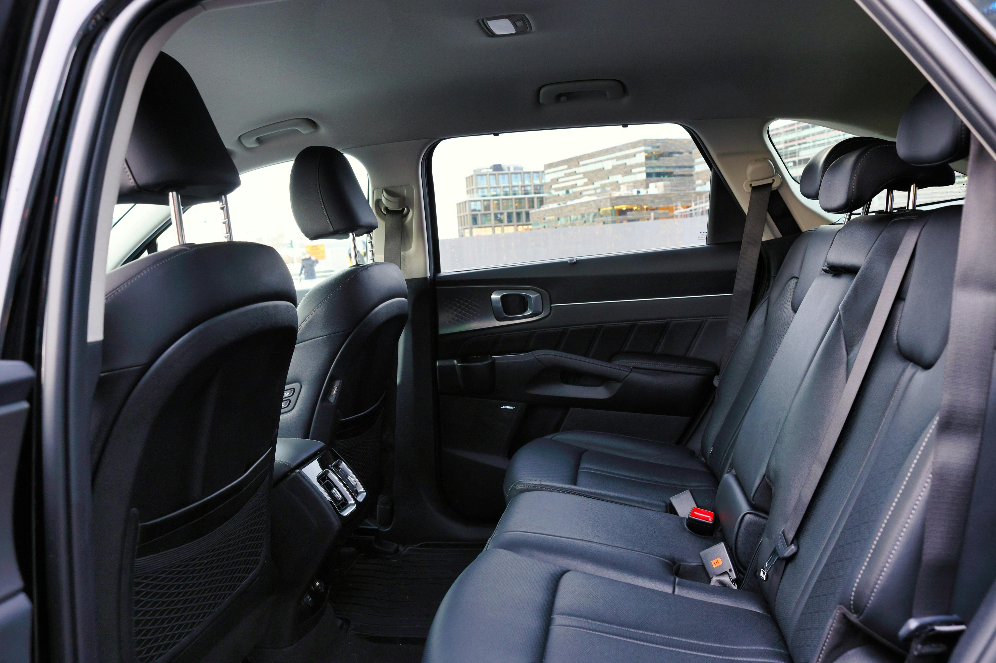 Rear seats of a modern car with black interior and city buildings visible through the windows.