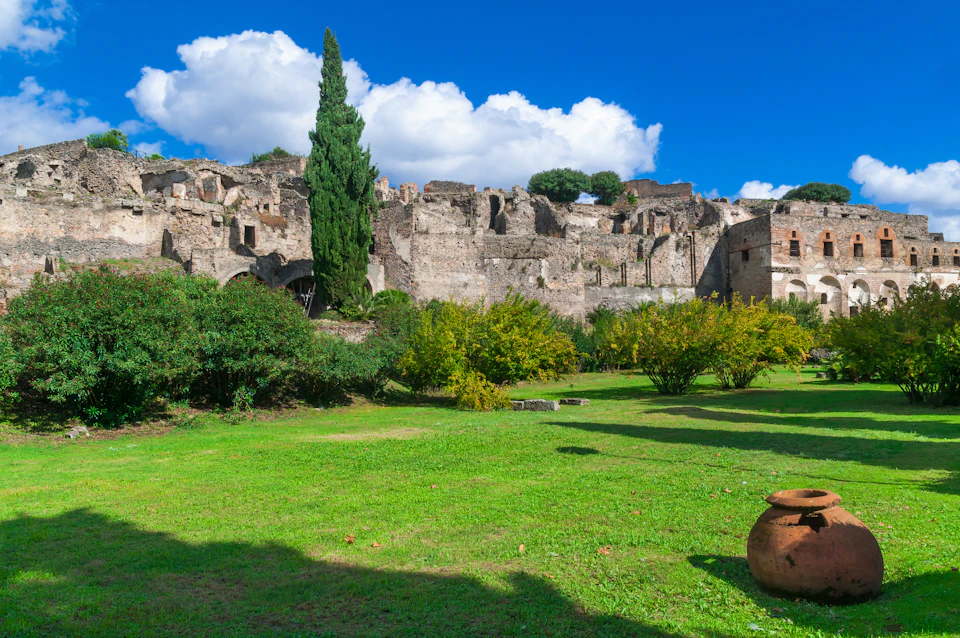 Ancient stone ruins surrounded by green bushes and trees under a bright blue sky with some white clouds.