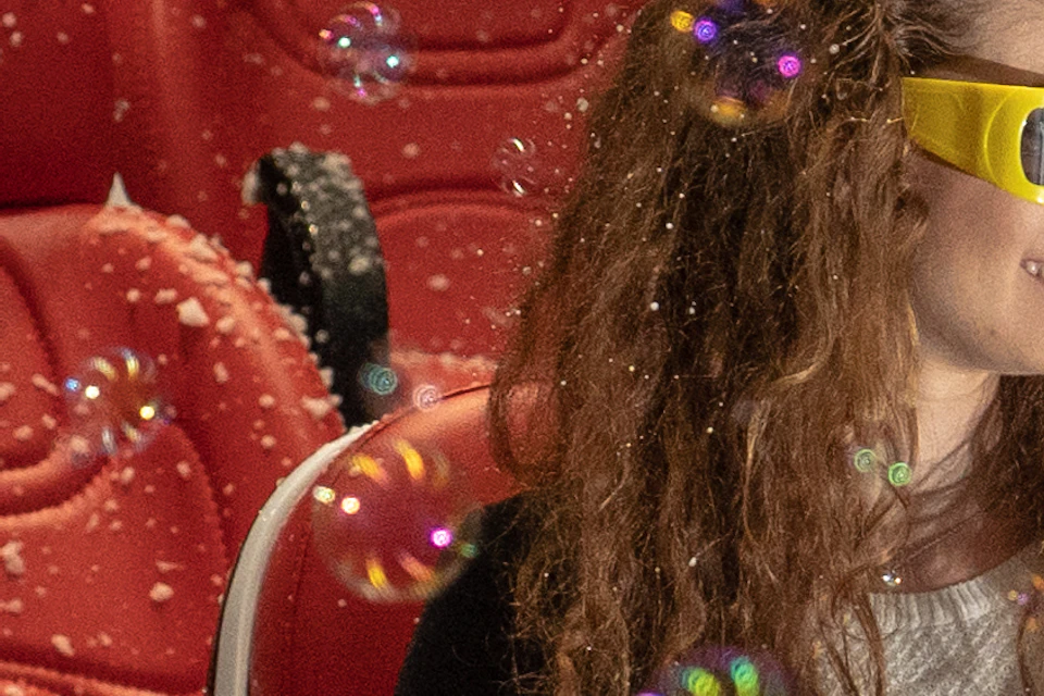 Three people wearing 3D glasses enjoy bubbles in a cinema with red seats.
