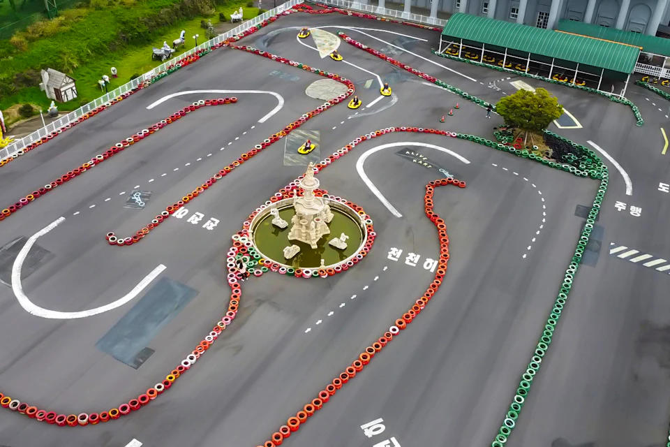 A go-kart track with winding lanes outlined by colorful tire barriers and a decorative fountain in the center.