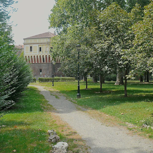 En park med en grusväg, träd, buskar, gatlyktor och en gul, historisk byggnad i bakgrunden.