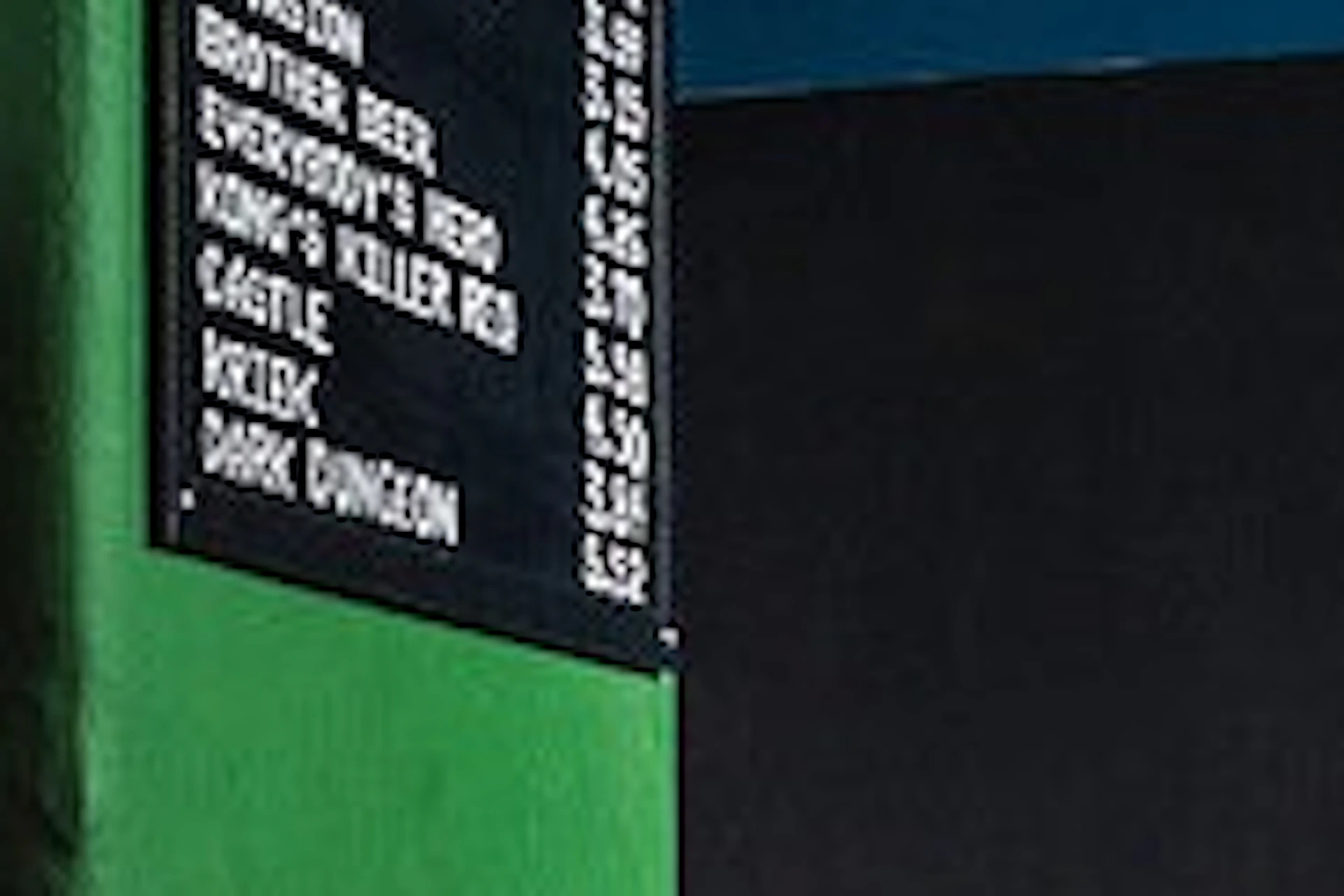 A man plays a retro arcade game while a woman peeks from a doorway in a bar-like setting with stools and a beer menu visible.