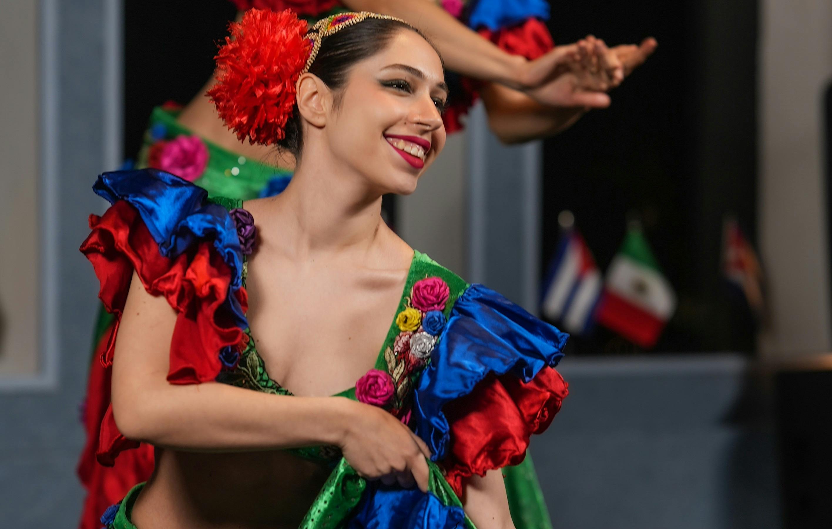 鮮やかな赤、青、緑の生地を着たカラフルな伝統的な服装の女性が、ダンスをしながら微笑んでいます。