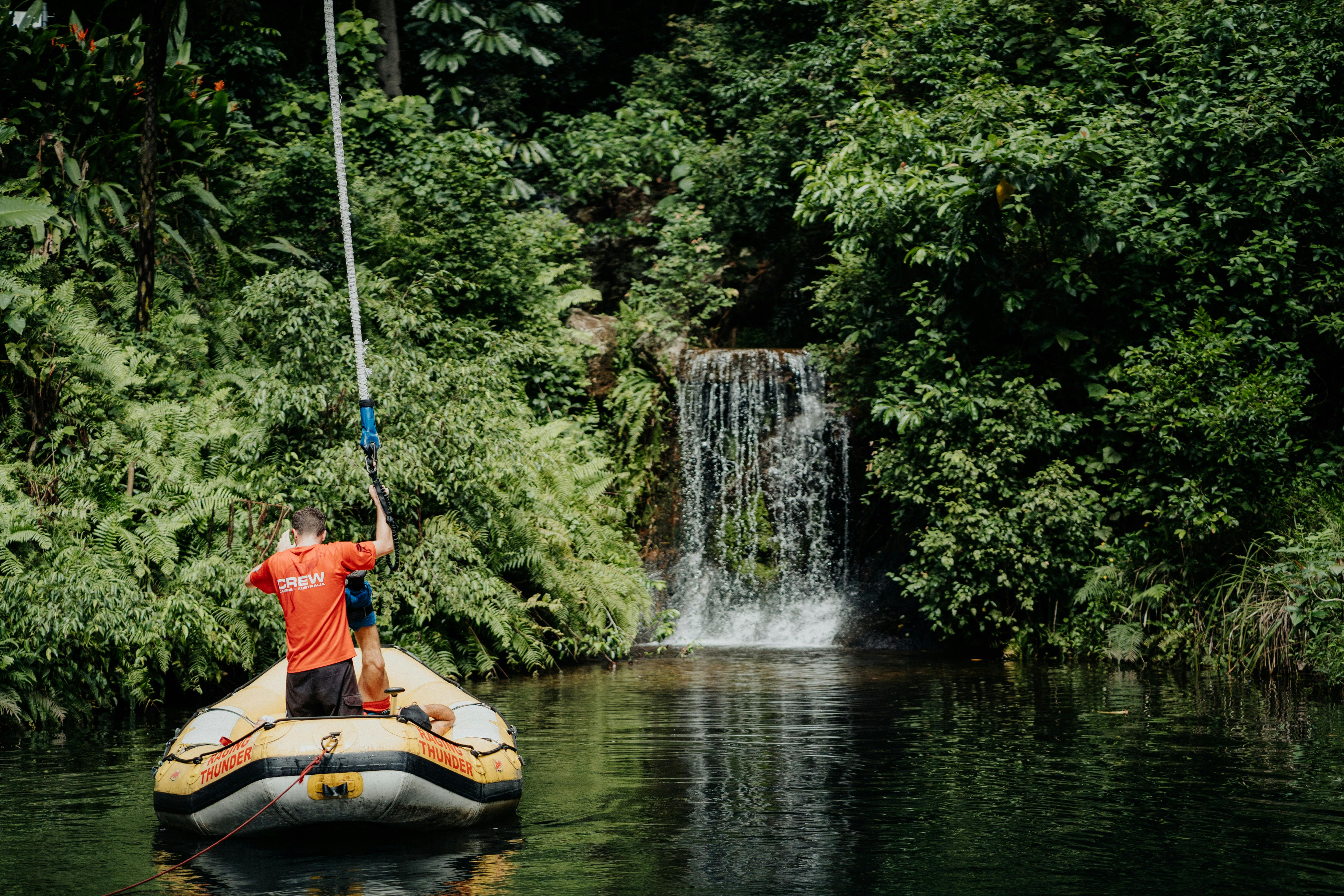 Person in a red shirt on a raft near a waterfall surrounded by dense greenery and trees.