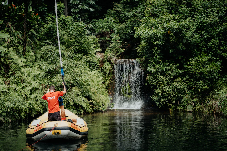 Person in a red shirt on a raft near a waterfall surrounded by dense greenery and trees.