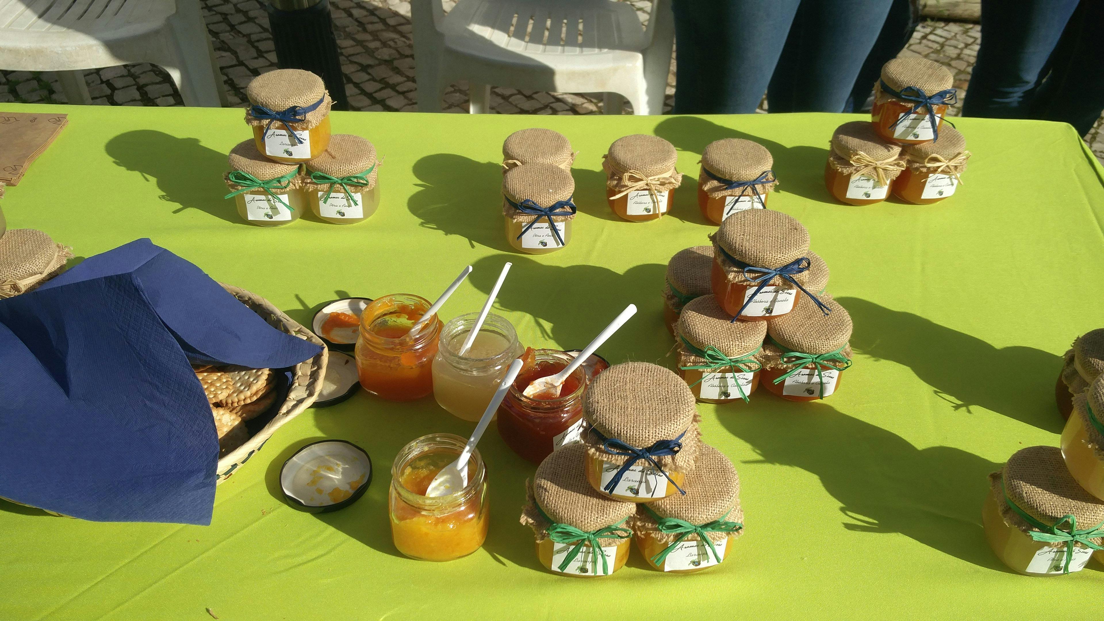 绿色桌布上有木盖和丝带的果酱罐，里面有一些罐子和勺子。 后面有一把椅子。