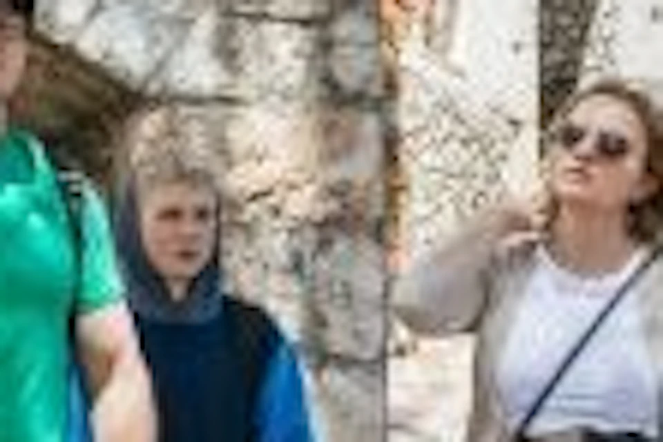 A tour guide speaks to a group of people in a stone courtyard with buildings in the background.