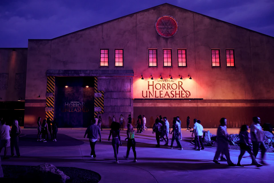 People walk outside a building with a sign reading "Universal Horror Unleashed" under purple lighting at dusk.