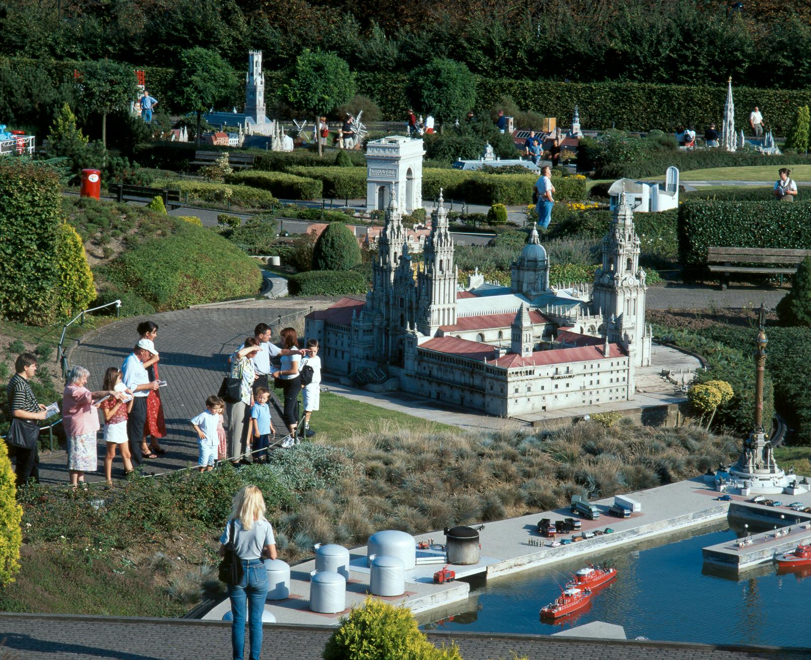 People observe detailed miniatures of famous landmarks, including an ornate cathedral and other buildings, in a landscaped park.