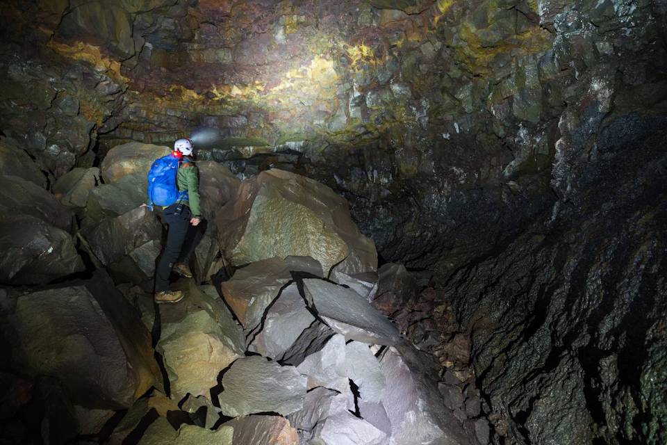 Person with a blue backpack and helmet with headlamp exploring a rocky cave.