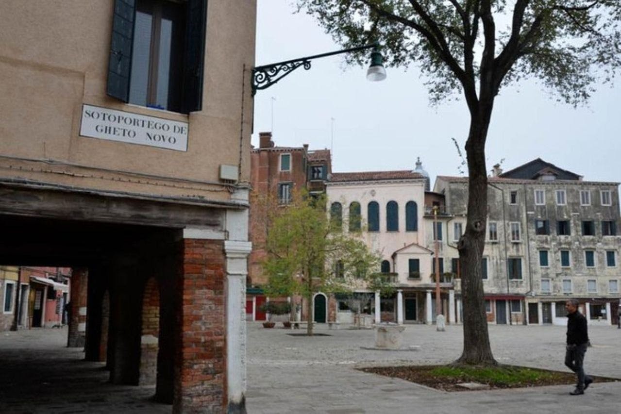 A quiet square with historic buildings, a tree, and a streetlamp in a European town.