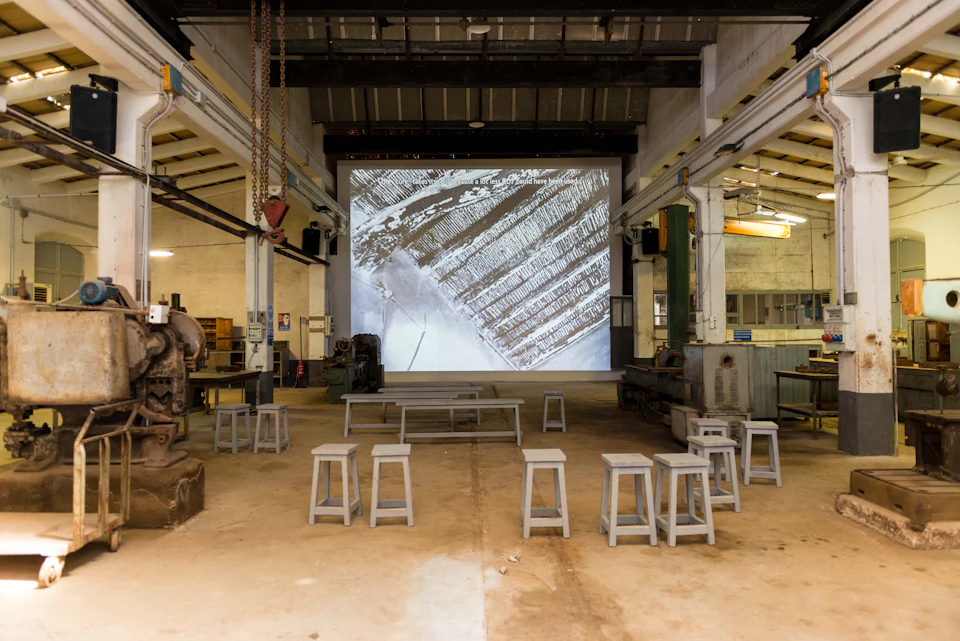 Spacious industrial room with stools arranged in front of a large screen displaying an aerial view of snowy fields.