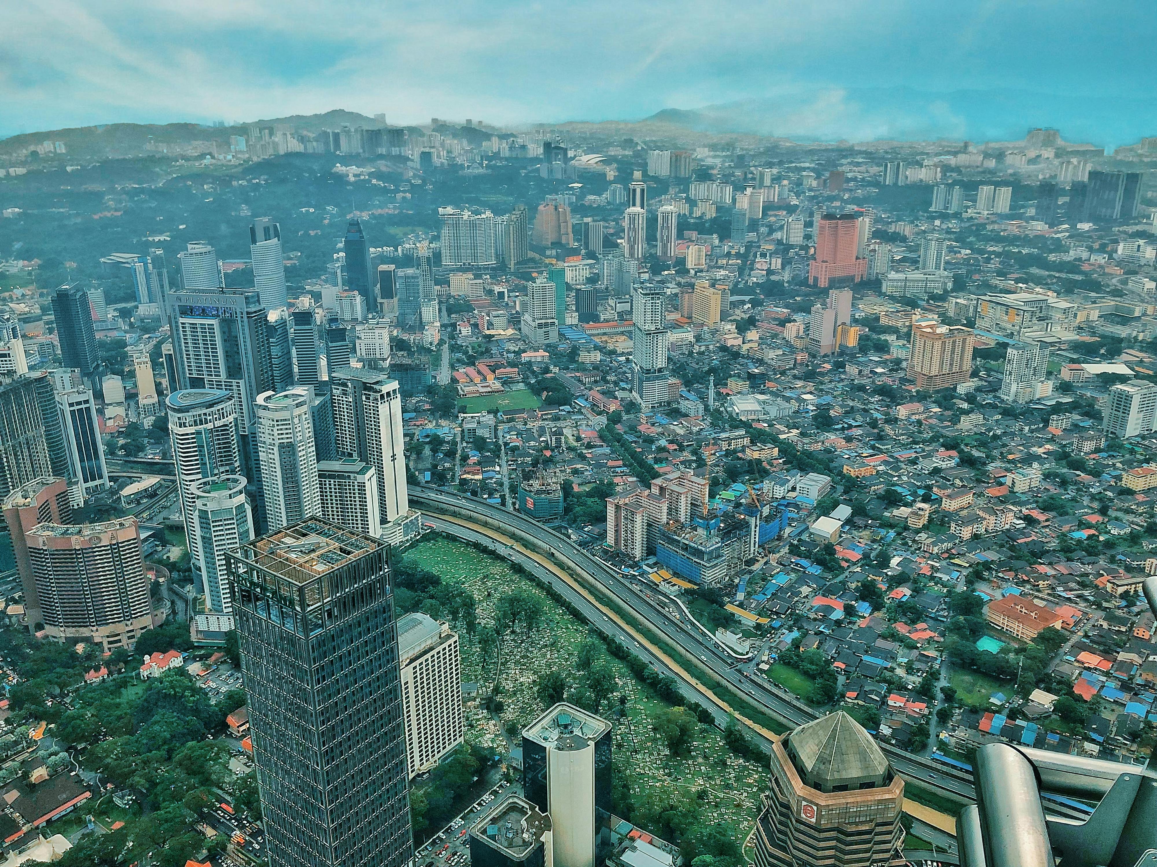 부분적으로 흐린 하늘 아래 자리한 수많은 고층 빌딩, 건물, 구불구불한 고속도로, 녹음이 우거진 도시의 공중 전망.