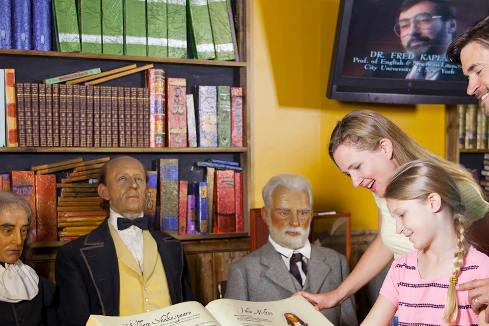 A family looks at a large open book with wax figures of historical figures behind them in a bookstore setting.
